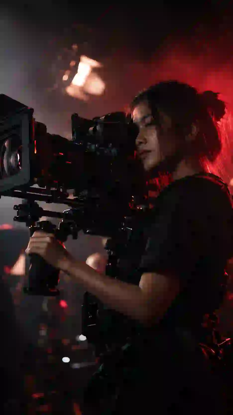 A camera operator with a shoulder-mounted cinema camera in red rim light.
