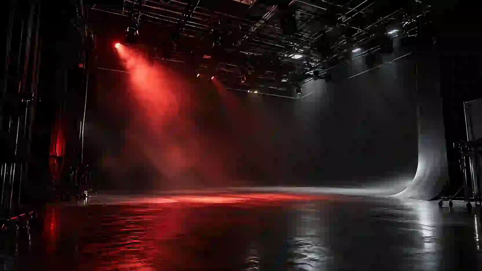 An empty black film studio, a single red light beam cutting through haze.